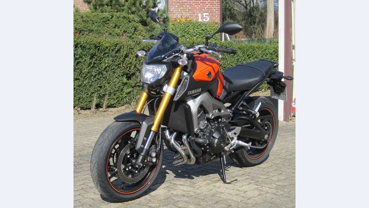 Yamaha MT-09 de première génération, orange et noire, garée devant une haie